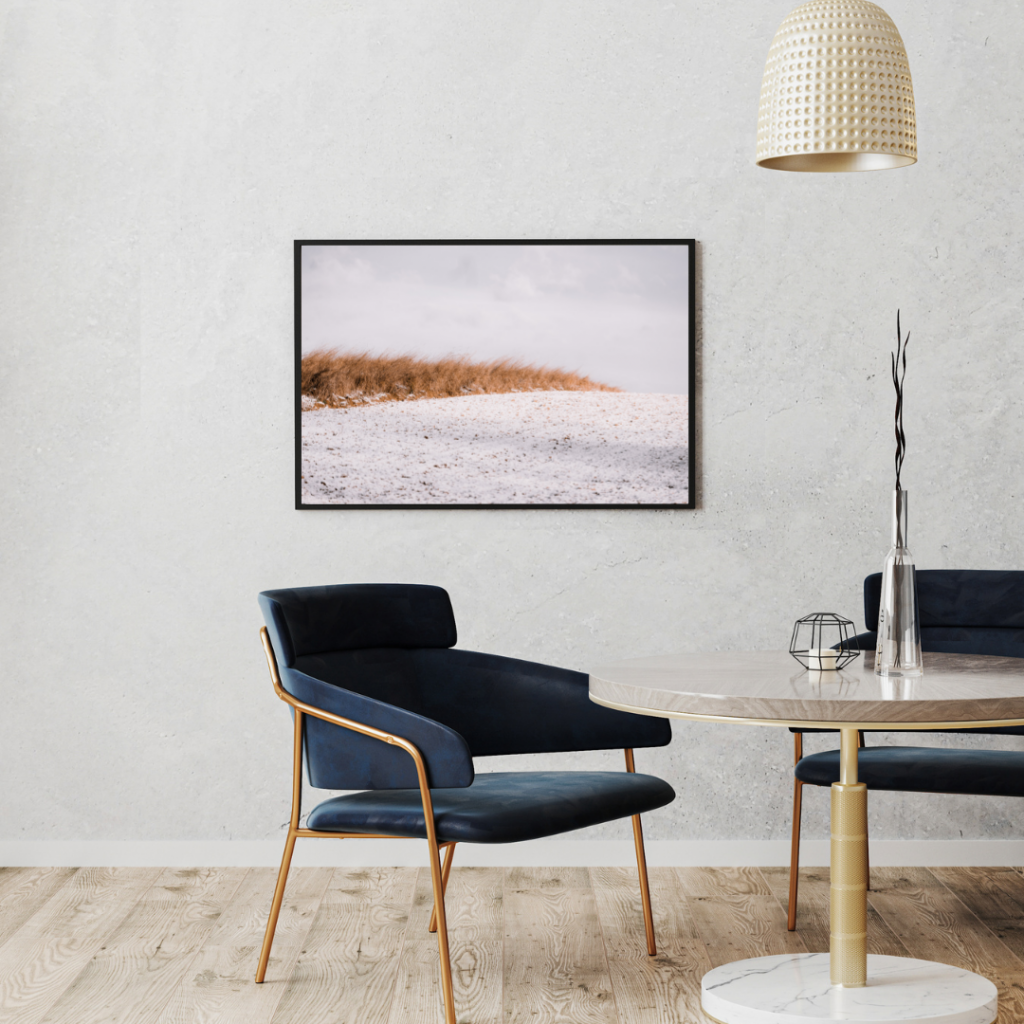Ein Wartezimmer das gemütlich mit einem Sessel und einen Tisch eingerichtet ist. An der Wand hängt ein gerahmtes Foto von Monoframe.