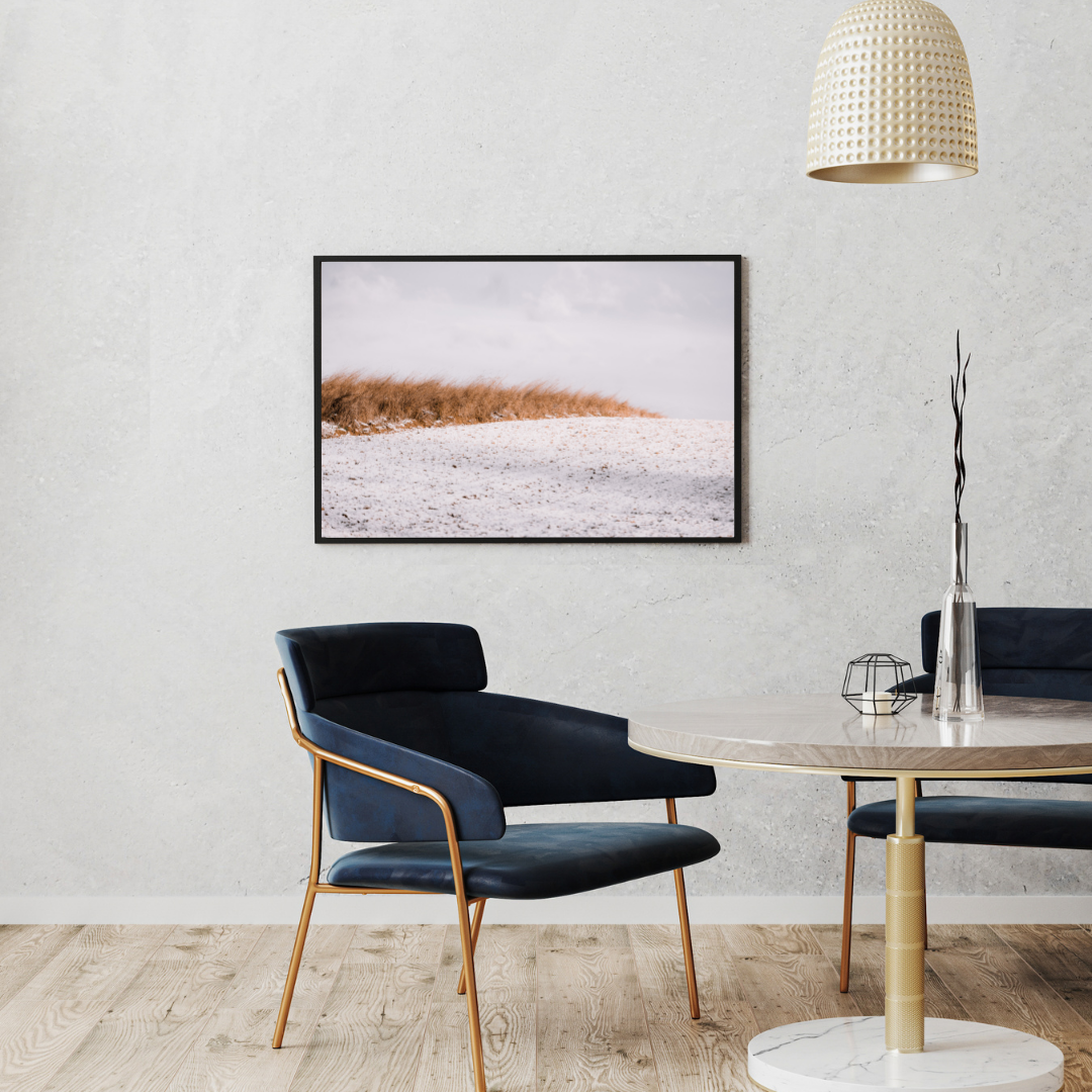 Ein Wartezimmer das gemütlich mit einem Sessel und einen Tisch eingerichtet ist. An der Wand hängt ein gerahmtes Foto von Monoframe.