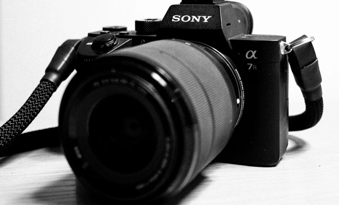 Eine Kamera, genauer, eine Sony A7R iii, liegt auf einer weißen Oberfläche, Es ist ein schwarz-weiß Bild, das Objektiv schaut nach vorne.
